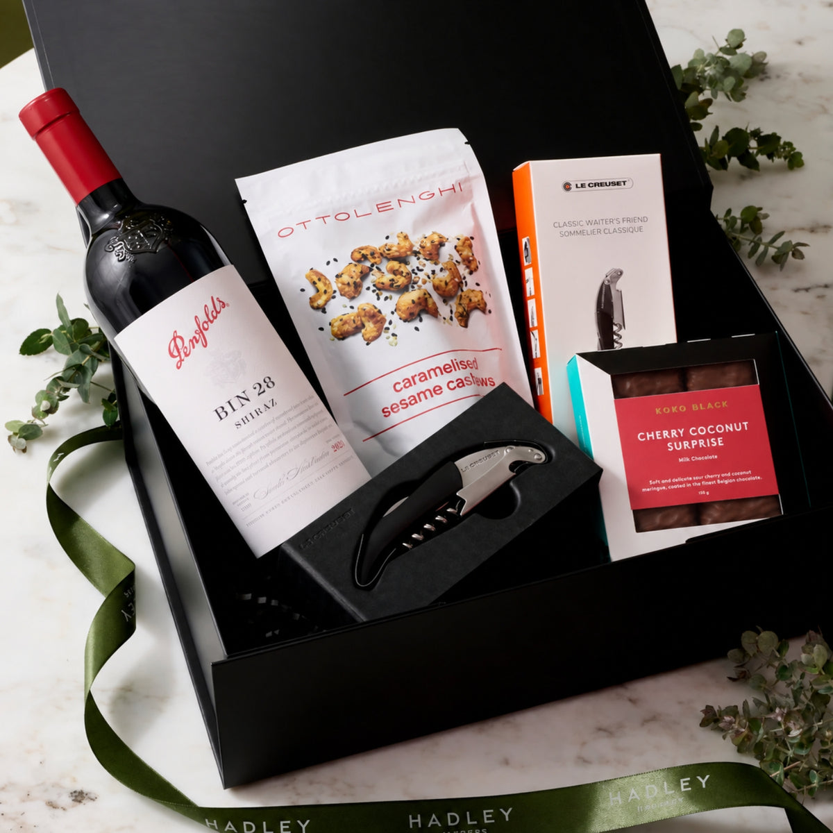 Shiraz Sophisticate hamper with Penfolds Bin 28 Shiraz, Ottolenghi cashews, Koko Black Cherry Coconut Surprise chocolate and Le Creuset corkscrew in a black gift box.
